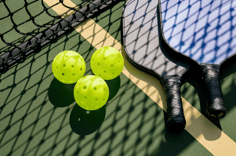 three pickleball balls with two paddleball racquets